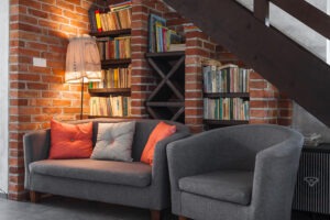 Two couches and a bookshelf against an interior brick wall