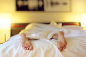 person lying on bed with covers covering whole body except for feet.