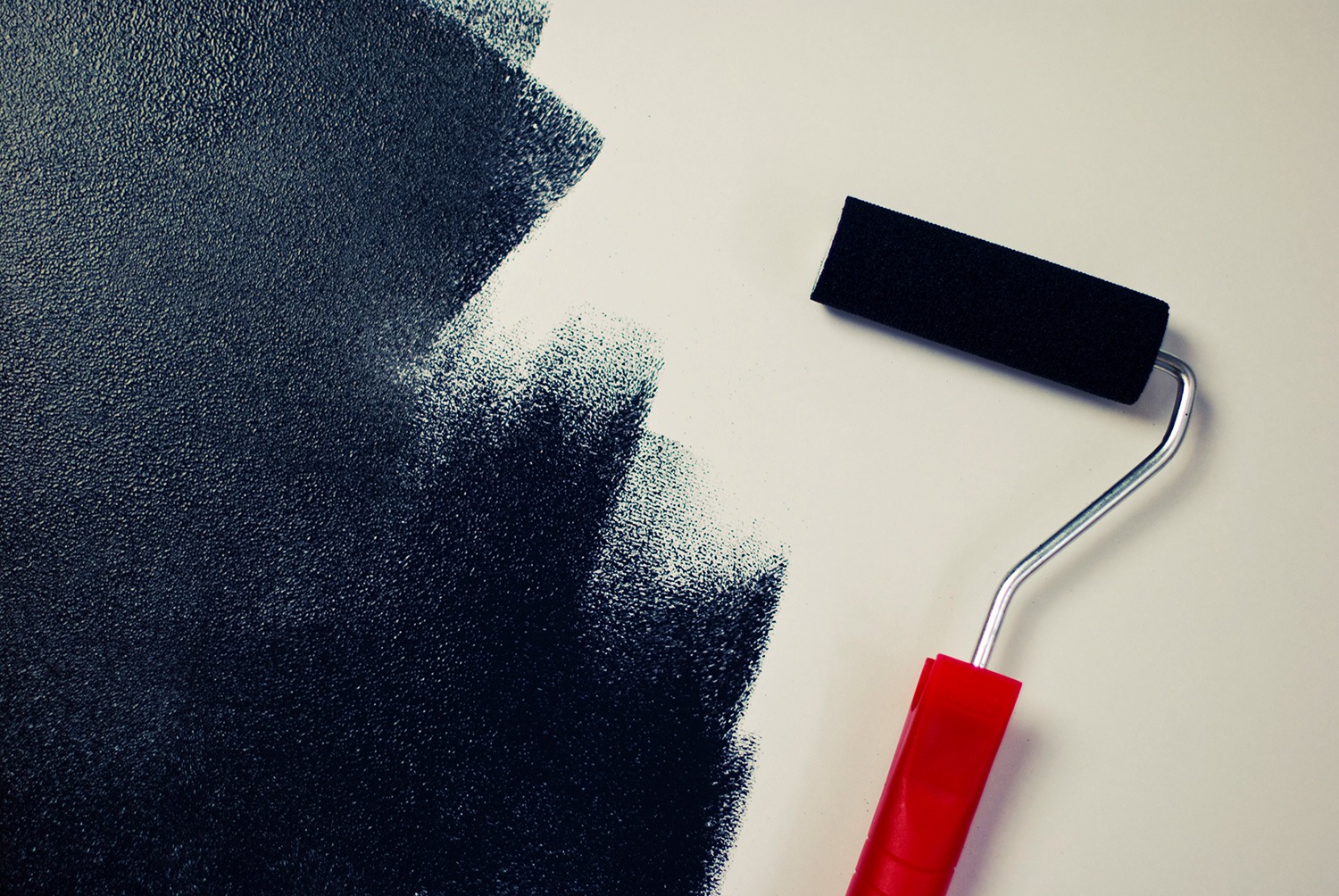 Paint roller rolling black paint onto a white wall